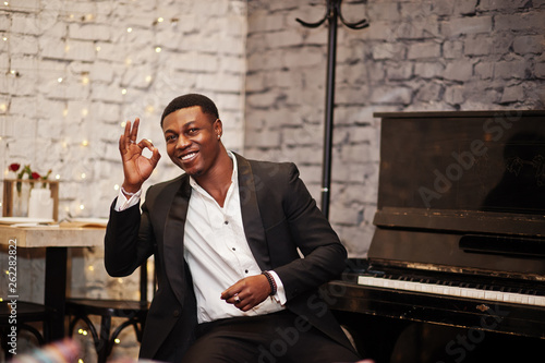 Photography Strong powerful african american man in black suit sitting against piano and show ok sign