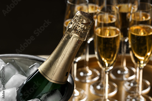Bottle of champagne in bucket with ice and glasses on table, closeup. Space for text