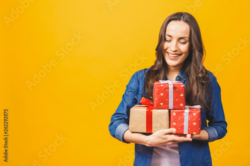 Young smiling model hold gift box. Woman isolated on yellow background.