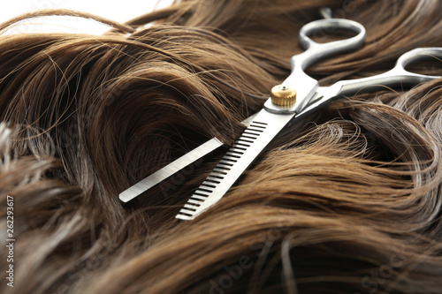 Thinning scissors on brown wavy hair, closeup. Hairdresser service