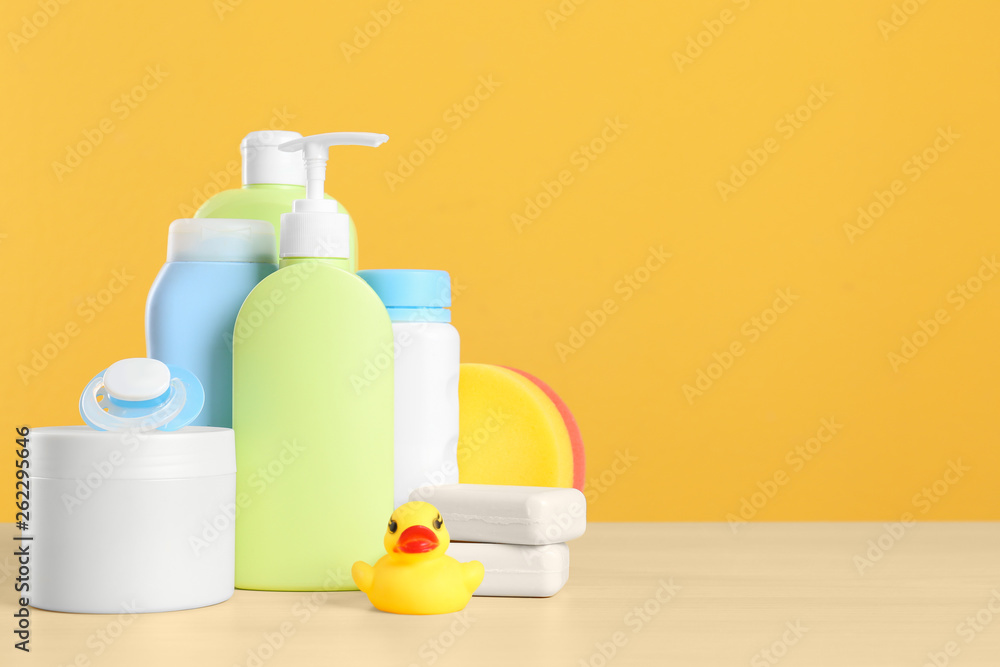 Baby cosmetic products, toy and pacifier on table against color background. Space for text Baby cosmetic products, toy and pacifier on table against color background. Space for text