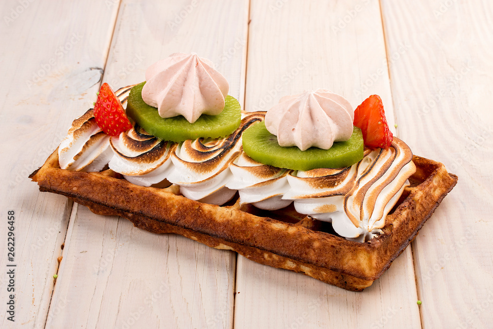Belgian waffle with meringue, strawberries and kiwi. On a light wooden background Belgian waffle with meringue, strawberries and kiwi. On a light wooden background