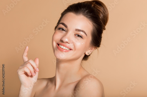 Happy smiling girl with perfect skin with moisturizing face cream on a cheek. Skin care and health concept.