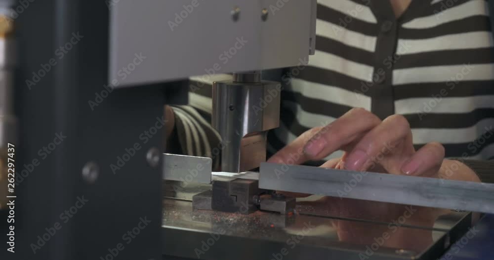 Industrial work in a garment factory. A woman seamstress prepares a fabric (zipper for clothes) for pressing and cutting fabric on a special machine for cutting and press. Concept of: Careful work. Industrial work in a garment factory. A woman seamstress prepares a fabric (zipper for clothes) for pressing and cutting fabric on a special machine for cutting and press. Concept of: Careful work.