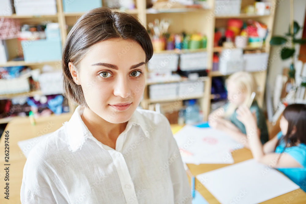 Pretty young woman smiling and looking at camera while standing on blurred background of classroom in art school Pretty young woman smiling and looking at camera while standing on blurred background of classroom in art school