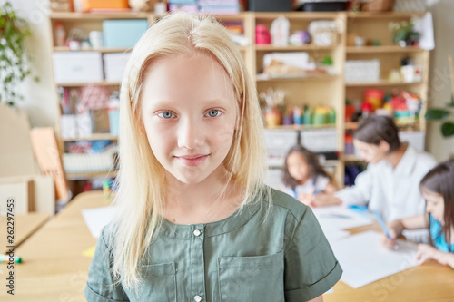 Lovely albino girl smiling and looking at camera while standing on blurred background of classroom in art school photo