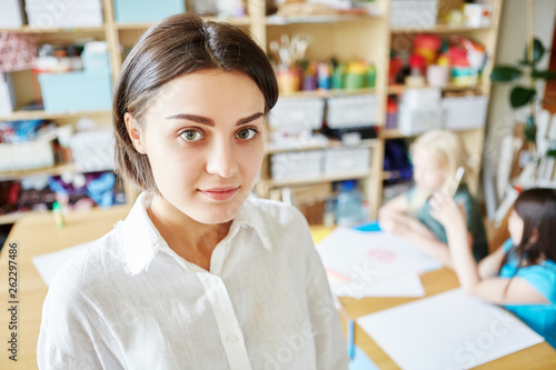 Pretty young woman smiling and looking at camera while standing on blurred background of classroom in art school