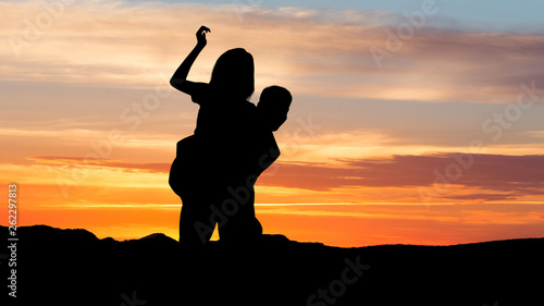 Couple at sunset. Silhouette of man piggybacking his girlfriend