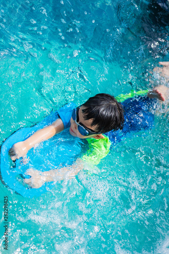 A boy is swimming with kickboard and swimming goggles.