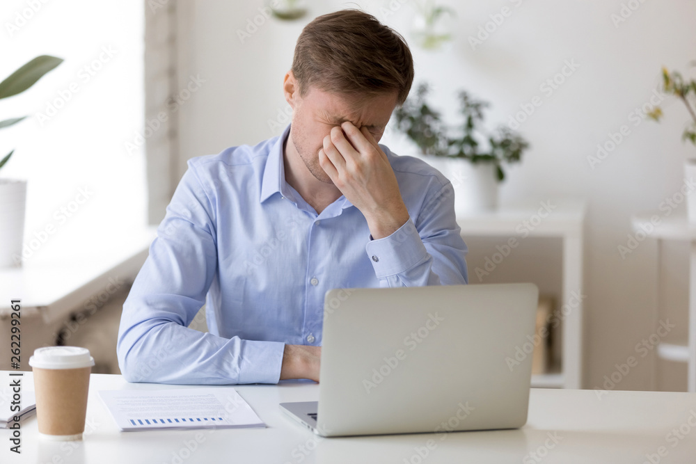 Millenial man massaging his nose at workplace Millenial man massaging his nose at workplace