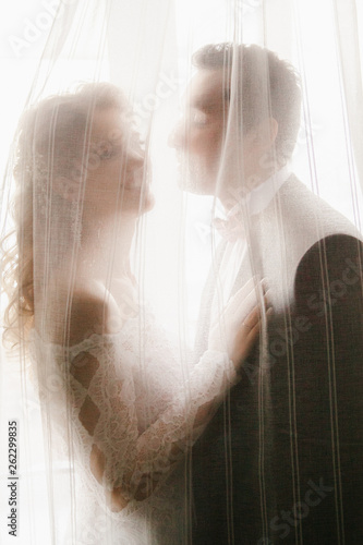 Happy wedding couple on the background of a white window in curtains