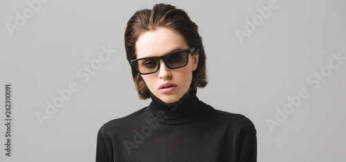 panoramic shot of attractive young woman in black sweater and sunglasses isolated on grey