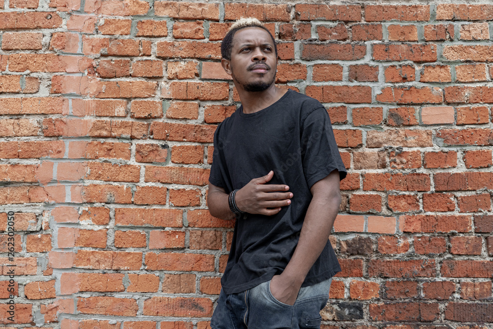 Young attractive dark-skinned man in black T-shirt on red bricked background. Young attractive dark-skinned man in black T-shirt on red bricked background.