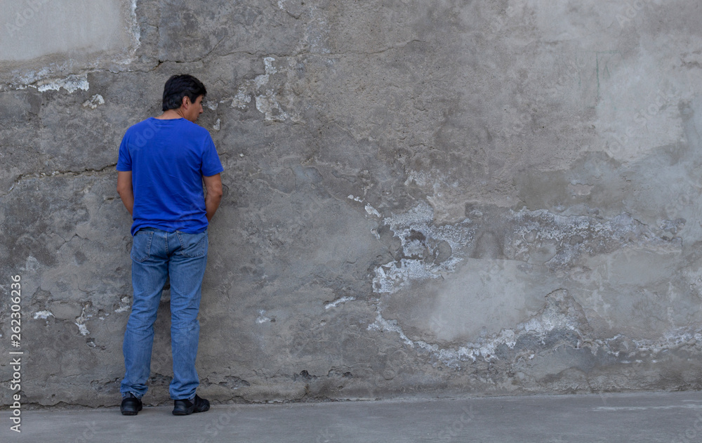 Man with blue shirt peeing on a wall