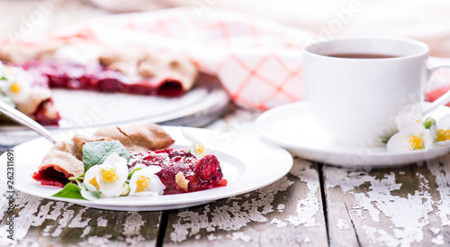 Piece of homemade deliciouse berry pie on a white plate with jasmine flowers and cup of tea on a wooden backgound. Copy space.