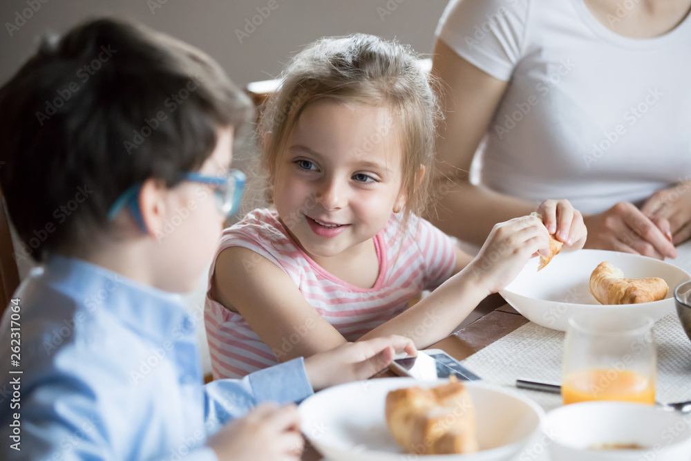 Smiling little girl talking with brother at breakfast at home