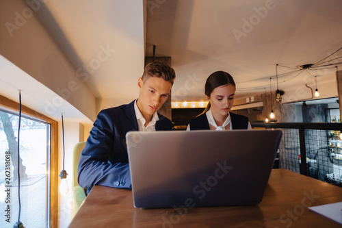 young businessmen boy and girl work with a laptop, a tablet and notes in the cafe