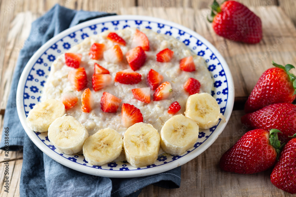 Oatmeal Porridge with Strawberries and banana on wooden rustic table. Healthy Breakfast with Fresh Organic Berries.