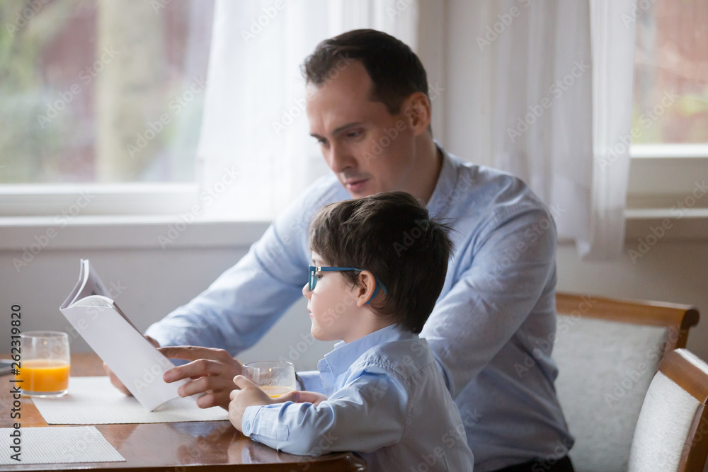 Father reading book to son aloud at kitchen at home Father reading book to son aloud at kitchen at home