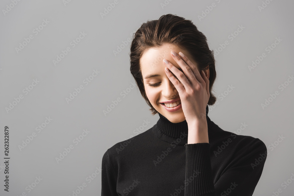 cheerful young woman in black jumper covering eye isolated on grey cheerful young woman in black jumper covering eye isolated on grey