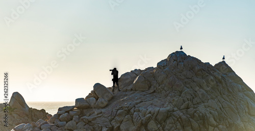 Photographer on cliff in silhouette on the coastline in Monterey Ca.