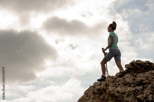 Young female hiker standing on the rocks with sticks