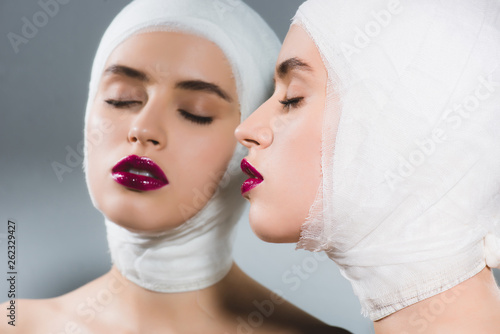 mirror reflection of attractive young woman with bandaged head and closed eyes on grey