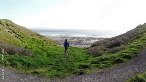 young man walking across field to get to beach beautiful 4k summer's day zoom over shoulder