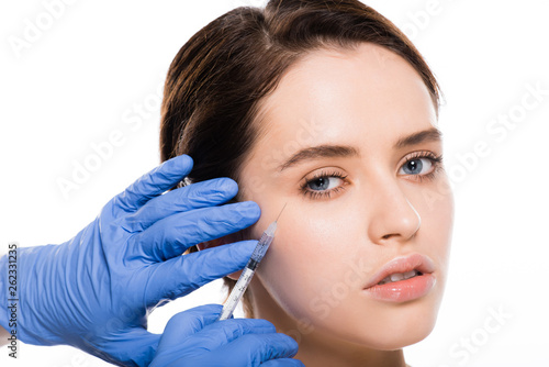 cropped view of cosmetologist in blue latex gloves holding syringe near face of young woman isolated on white