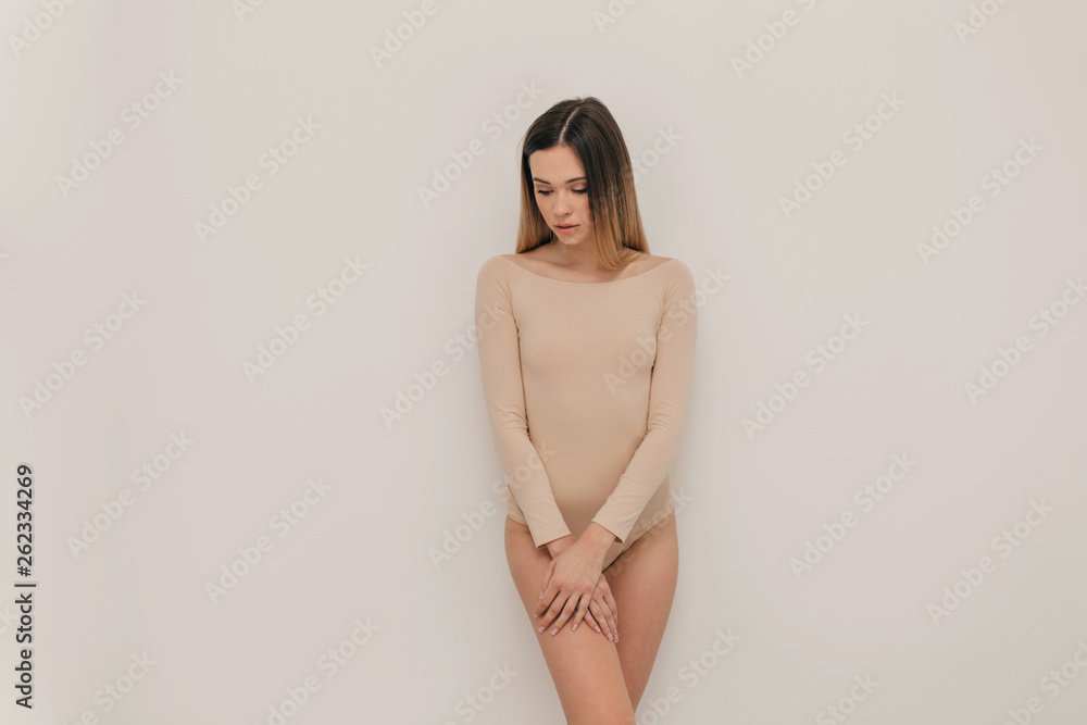 Cute natural woman standing over white wall dressed in beige body and enjoying life Cute natural woman standing over white wall dressed in beige body and enjoying life