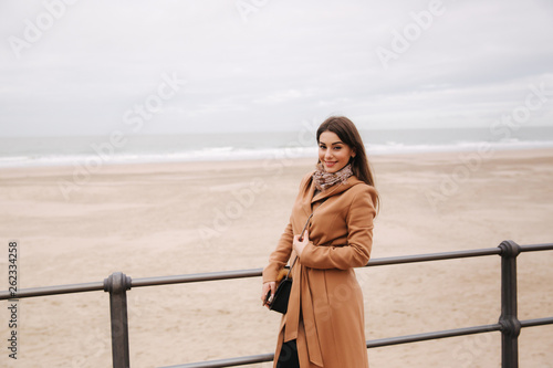 Stylish lady with make up in beautiful coat standing along North Sea. Woman smile