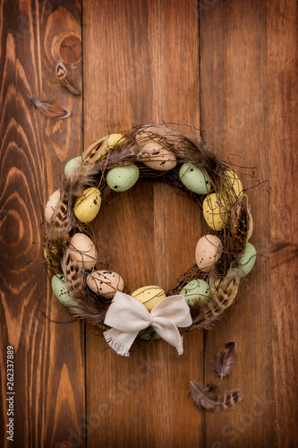 Isolated vine wreath is decorated with bird feathers, quail eggs, on the brown wooden background, Easter scene, composition.