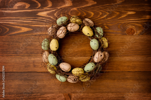 Isolated vine wreath is decorated with quail eggs, on the brown wooden background, Easter scene, composition.