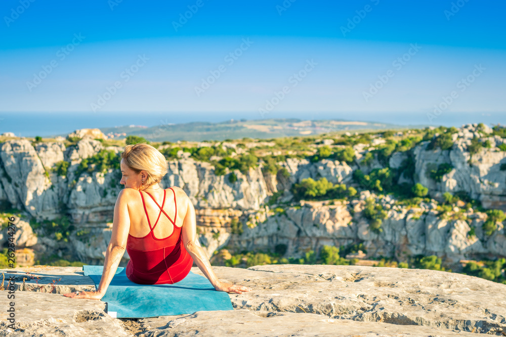 Yoga Fitness Woman Resting and Enjoying View after Training Session. Sitting at the Edge of Cliff Overlooking Mountain Range and Ocean in Far Distance. Yoga Fitness Woman Resting and Enjoying View after Training Session. Sitting at the Edge of Cliff Overlooking Mountain Range and Ocean in Far Distance.