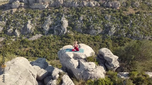 Aerial Footage of Mature Yoga Fitness Woman Performing Half Lotus (Ardha Padmasana) with Hands Together, Sitting on Cliff at Ravine Edge. Zoom From Horizontal to Rocket Viewpoint.