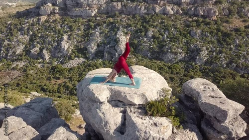 Aerial Footage of Mature Yoga Fitness Woman Performing Downward Facing Dog (Adho Mukha Svanasana) Pose with One Leg. Standing on a Cliff at Edge of Ravine. Circling Around Model.
