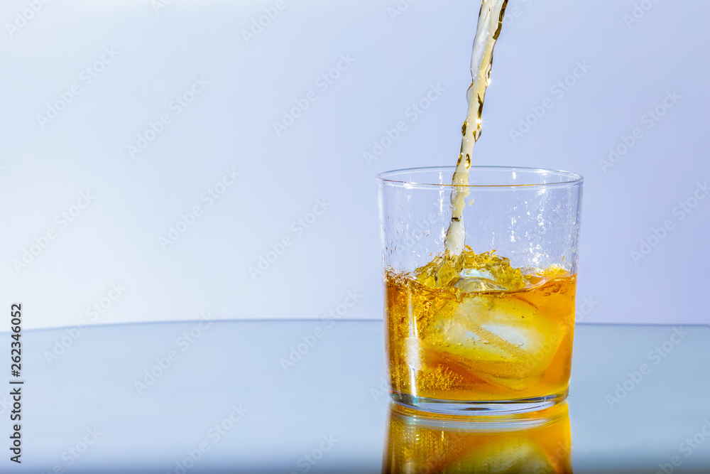 Whiskey pours into a glass of ice and whirls around, against a neutral blue background Whiskey pours into a glass of ice and whirls around, against a neutral blue background