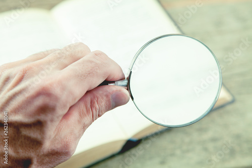 Man using magnifying glass for reading the book.