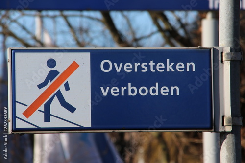 Blue and white sign with dutch language text  oversteken verboden  which means that trespassing the rails is not allowed