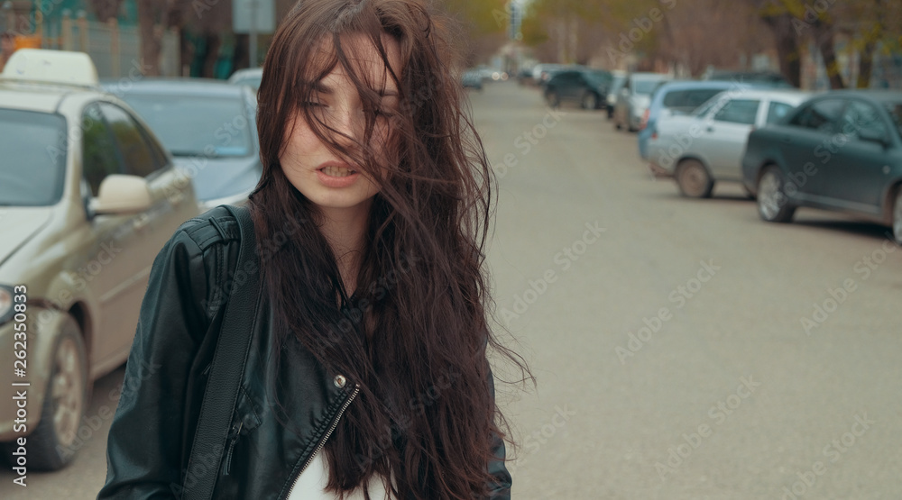 Girl in windy day with blowsy hair in the street with parked cars