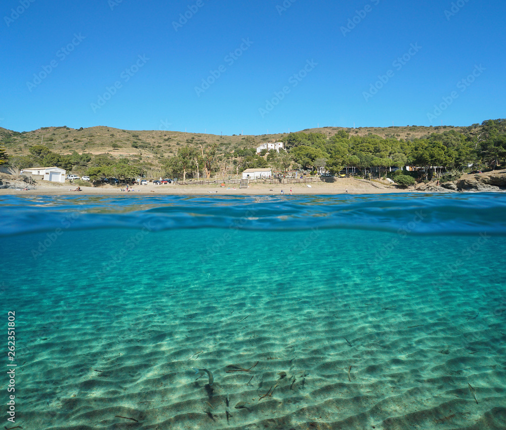 Spain peaceful beach with sandy seabed on the Mediterranean coast, split view half over and under water, Roses, Costa Brava, Catalonia