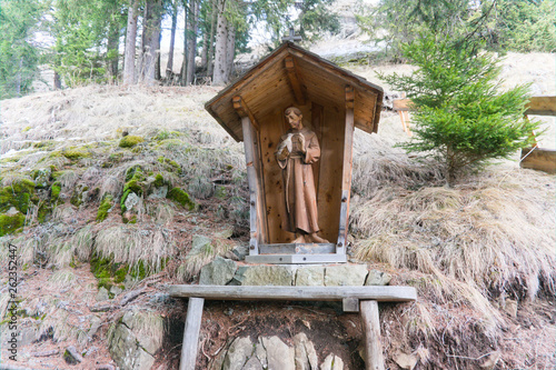 A wood carved catholic statue of a holy monk in the forest of tyrol in the dolomites photo