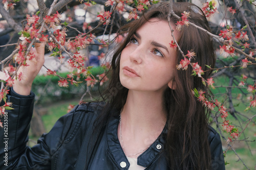 Thoughtful girl posing outdoors with her eyes looking away of camera while standing near blooming cherry tree