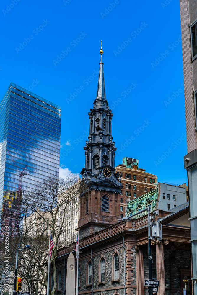 Fototapeta premium St. Paul's Chapel of Trinity Church Wall Street in the background is Seven World Trade Center with clouds and construction crane reflected in the windows .