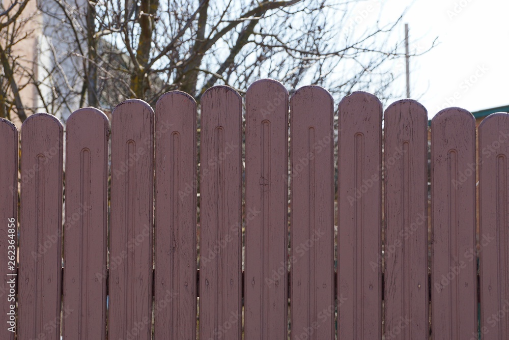 part of a brown wooden fence from a row of planks against a background of branches and sky part of a brown wooden fence from a row of planks against a background of branches and sky