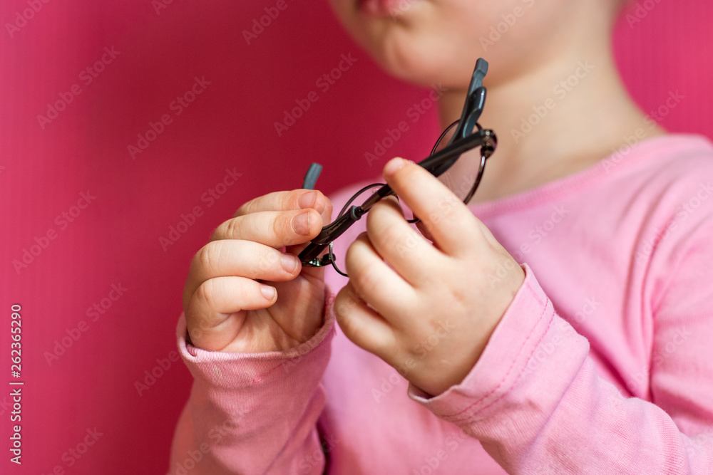 Happy blond child posing in room over pink background. Kid takes off and puts on glasses for fitting