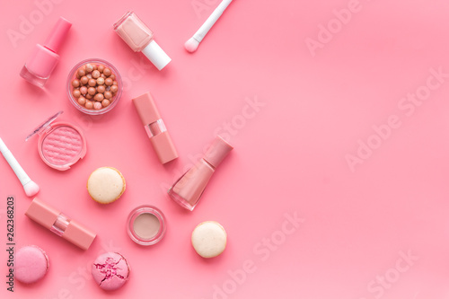 Make-up artist desk with powder, nail polish, decorative cosmetics and macaroon cookies pink background top view mokeup