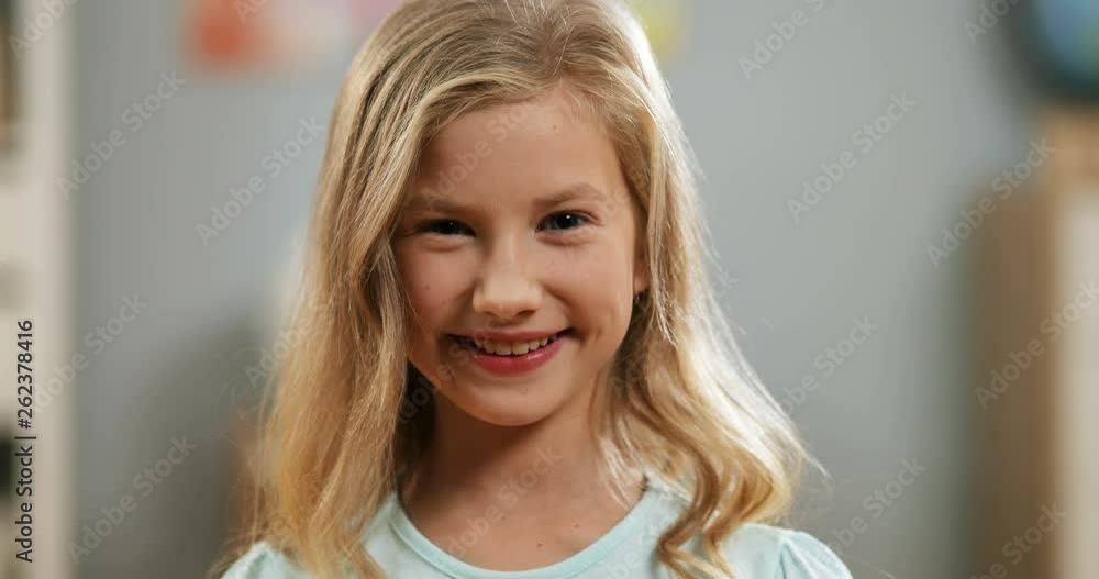 Close up of the pretty blond Caucasian small girl smiling cheerfully to the camera at home. Portrait. Close up of the pretty blond Caucasian small girl smiling cheerfully to the camera at home. Portrait.