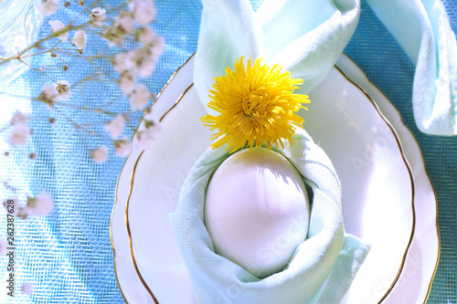 Easter table setting. Egg in a napkin decorated with a dandelion on a plate, in the form of leaves...