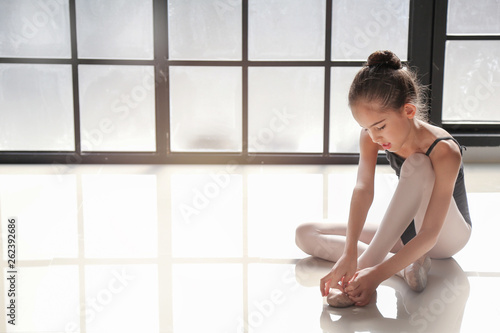 9 years old girl was sitting on the floor and tying ballet shoes for ballet class practice with the light from window background.